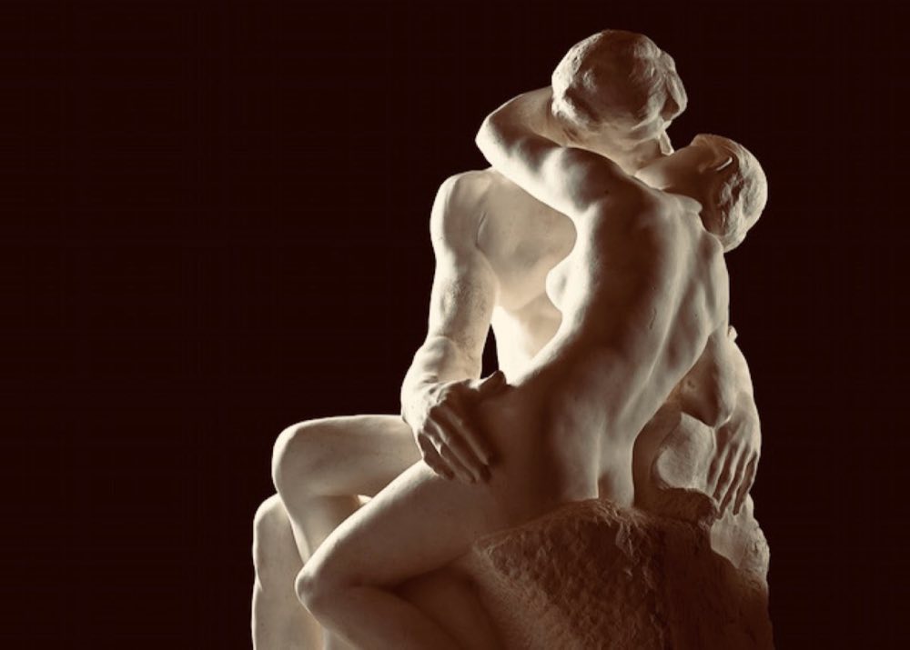 A white sculpture of two lovers embracing against a dark background